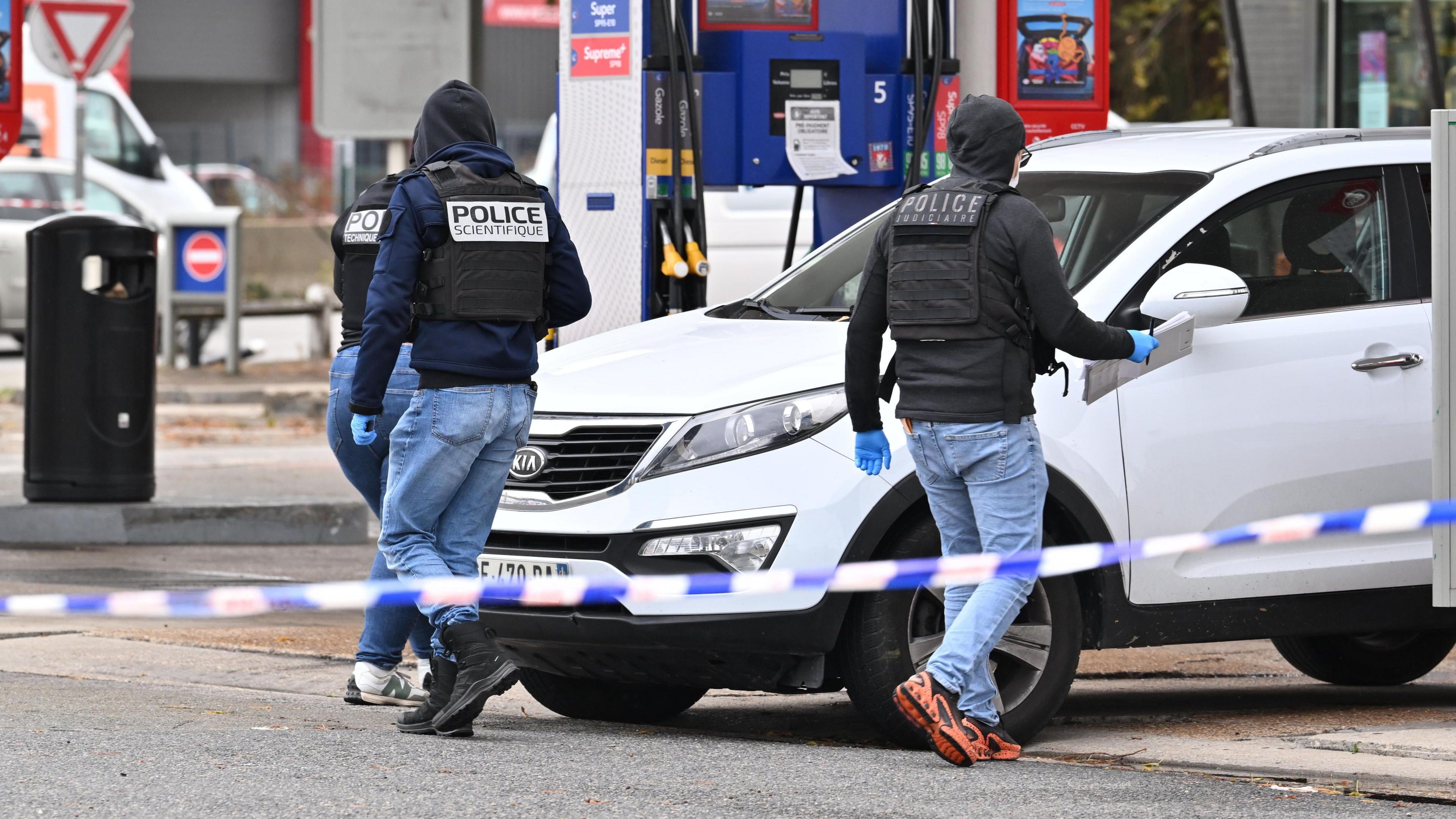 Forensic officers examine evidence at the site of a petrol station where a gunman opened fire from a vehicle, killing one person and injuring four others